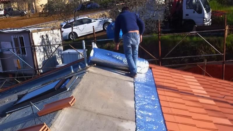 מתקין פורש יריעת בידוד רפלקטיבית על גג רעפים במהלך עבודת התקנה באתר