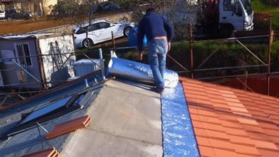 מתקין פורש יריעת בידוד רפלקטיבית על גג רעפים במהלך עבודת התקנה באתר