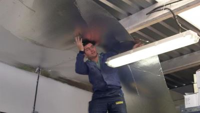 מתקין מצמיד יריעת בידוד רפלקטיבית לתקרת פנים במבנה עבודה