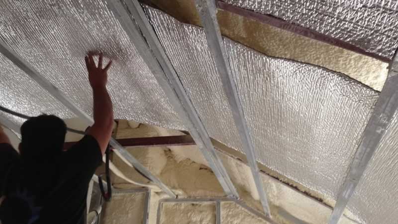 מתקין מצמיד יריעת בידוד רפלקטיבית בין קורות מתכת בעליית גג