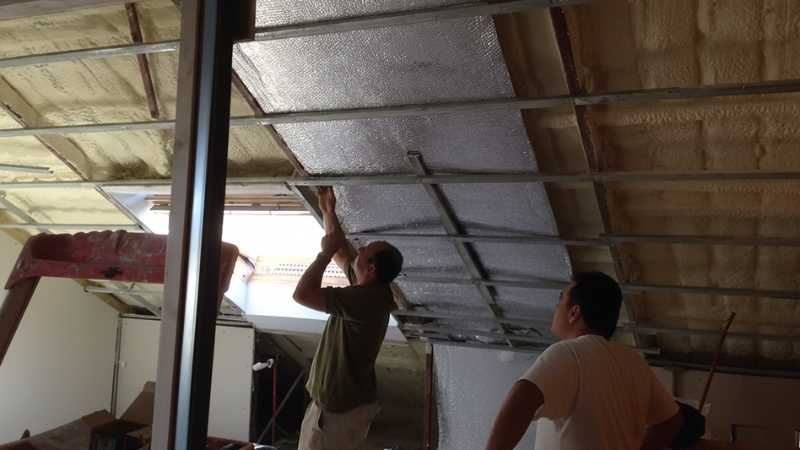 לחיצה להגדלת תמונה שני מתקינים מצמידים יריעת בידוד רפלקטיבית לתקרה בעליית גג עם קורות וקצף מוקצף