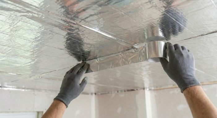 לחיצה להגדלת תמונה אדם מדביק סרט מטאלי דביק על תקרה מבודדת ביריעות בידוד תרמי.